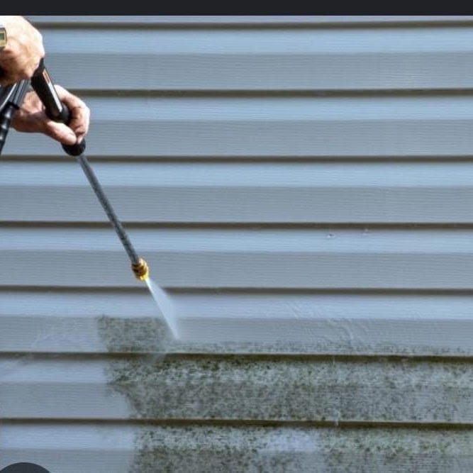 A pressure washer wand cleaning green algae off vinyl siding