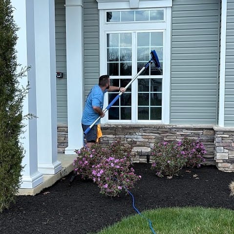 M&J technician cleaning a front window on a siding home